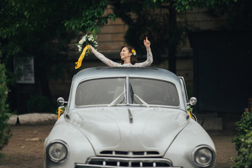 Stylish happy bride inside of retro car. Emotional moment. 