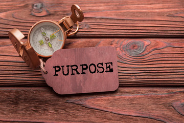 Purpose written on a wooden tag, tourist compass on a wooden background. tourism, the achievement of objectives.