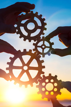 Gears in the hands of people on the background of the evening sky. the mechanism of teamwork. interaction.