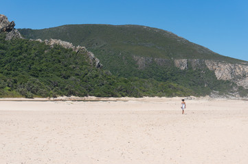 Fototapeta na wymiar Woman in a summer hat and dress walking on the sand