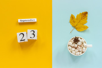 Autumn composition. Wooden calendar September 23, cup of cocoa with marshmallows and yellow autumn leaves on yellow blue background. Top view Flat lay Mockup Concept Hello September