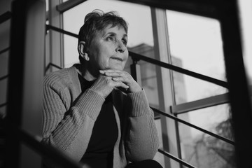 Poor senior woman sitting on stairs indoors. Black and white effect