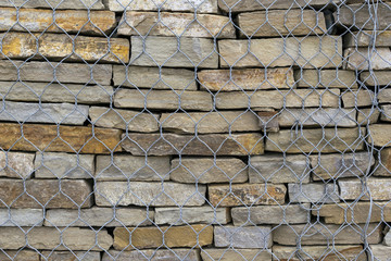 The construction of the wall of natural stone. The stone slabs are stacked on top of each other. A pile of natural stone is fenced with a metal mesh.