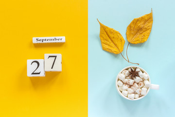 Autumn composition. Wooden calendar September 27, cup of cocoa with marshmallows and yellow autumn leaves on yellow blue background. Top view Flat lay Mockup Concept Hello September.