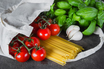 Reusable bag with groceries. Tote bag, minimal waste. Fresh basil, tomatoes cherry, garlic in fabric bag on dark table background. Top view, copy space.
