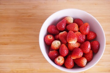 Strawberries in white ceramic bowl. Fresh nice strawberries on wooden table.