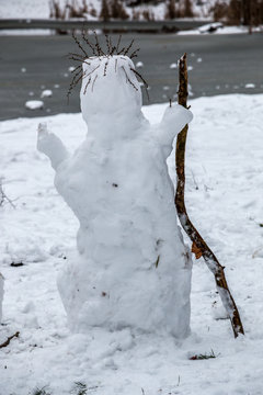 White snowman mit a wooden stick and hair made of dry grass