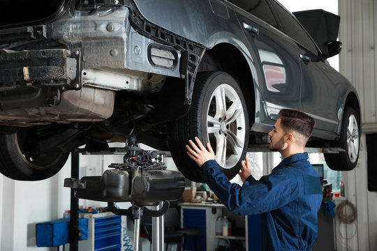 Technician checking car on hydraulic lift at automobile repair shop