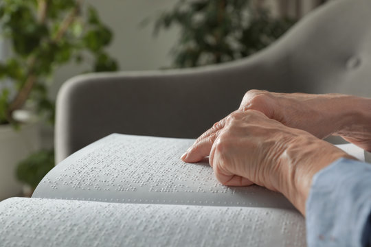 Blind senior person reading book written in Braille on sofa indoors, closeup