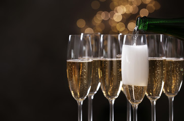 Pouring champagne into glasses on blurred background, closeup. Space for text