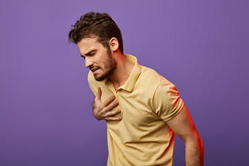 weak sick guy having problems with heart. attractive unhappy man in yellow T-shirt touching his...