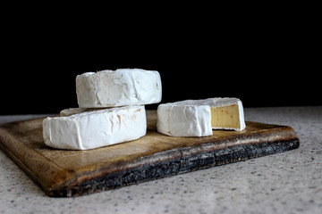 Three heads of cheese with white mold on the wooden surface. Delicious brie, Camembert, goat. Round shape. Cutting Board is textured, opalinum edge.