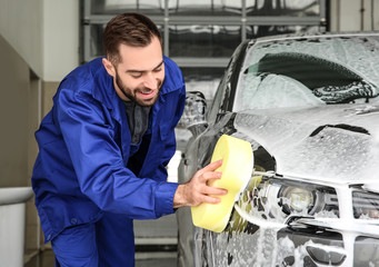 Worker cleaning automobile with sponge at professional car wash