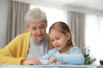 Cute girl and her grandmother reading book at home