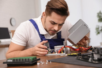 Male technician repairing power supply unit at table indoors