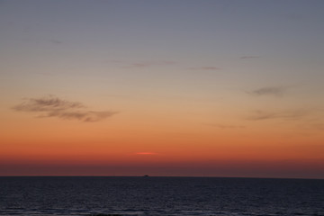 Red and blue colors in the sky by the ocean with a ship at the horizon