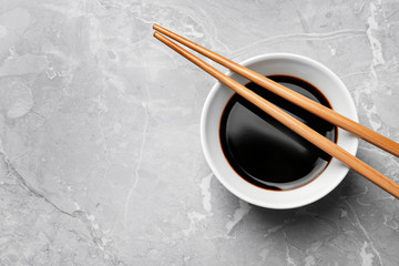 Bowl of soy sauce with chopsticks on marble background, top view. Space for text