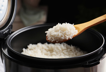 Spoon with tasty hot rice over cooker, closeup