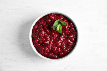 Bowl of tasty cranberry sauce with sauce on white wooden background, top view