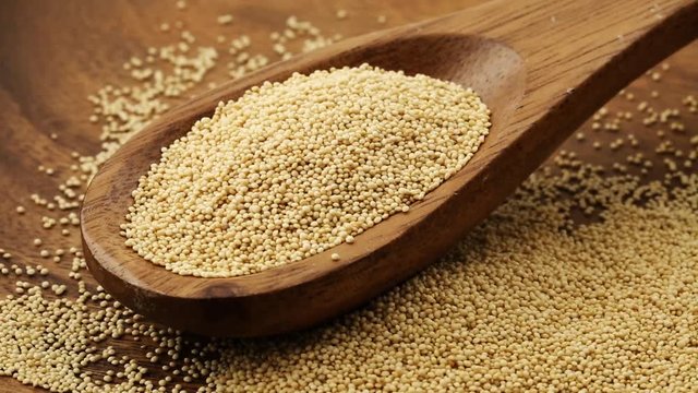 Heap of raw, uncooked amaranth seeds in wooden scoop rotating