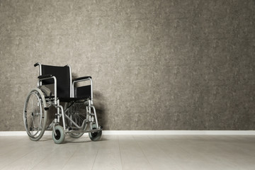 Empty wheelchair near grey wall indoors. Space for text