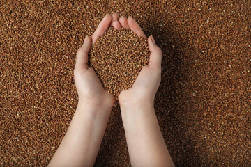 Closeup of woman holding raw buckwheat over grains, top view