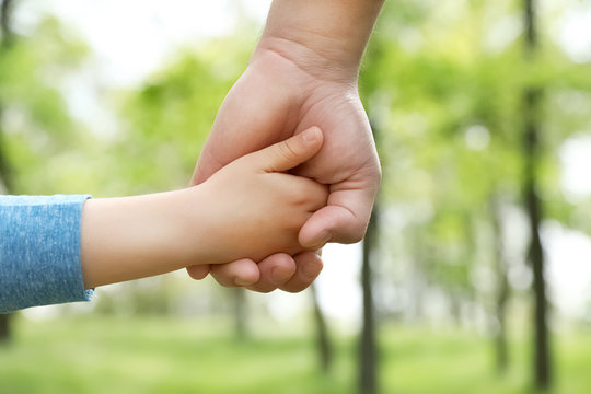Little child holding hands with his father outdoors, closeup. Family time