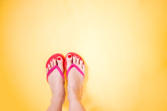 Woman's legs wearing pink flip flops on yellow background with copy space