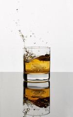 Golden brown liquor splashing with ice in a glass and reflecting on the table’s surface