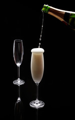 A bottle over pouring champagne into one of two champagne flutes on a black background