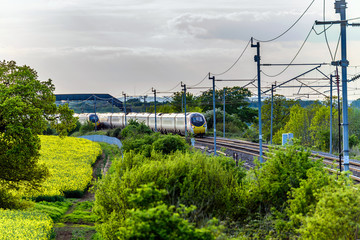 uk train railroad next to rapeseed field in bloom day view in england. spring railway landscape