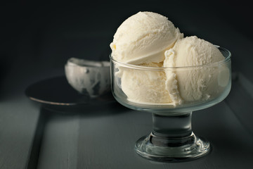 Closeup of ice cream balls in a glass vase on a gray wooden background and a spoon on a dish in the background