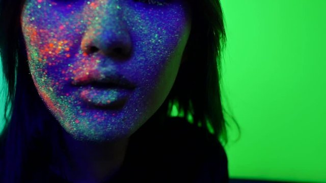  Beautiful young woman dancing and making party with fluorescent painting on her face. Neon facial portraits