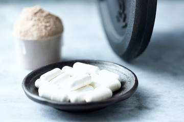 Beta-alanine capsules, Scoop of Whey Protein and a dumbbell in background. Sport nutrition. Stone / Wooden background. Copy space