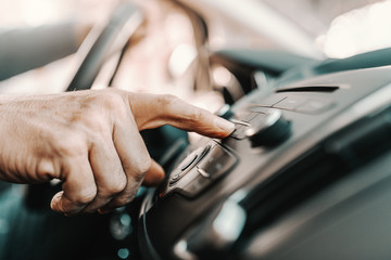 Close up of senior man changing radio station while sitting in his car.