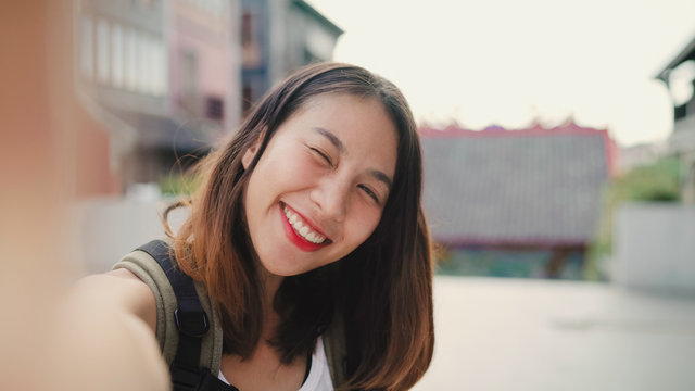 Cheerful beautiful young Asian backpacker blogger woman using smartphone taking selfie while traveling at Chinatown in Beijing, China. Lifestyle backpack tourist travel holiday concept. Point of view.