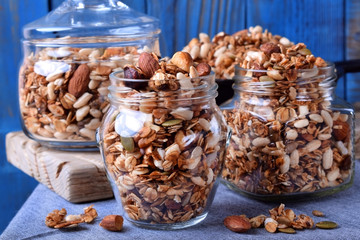 Homemade granola with different nuts and seeds in glass jars against the blue background
