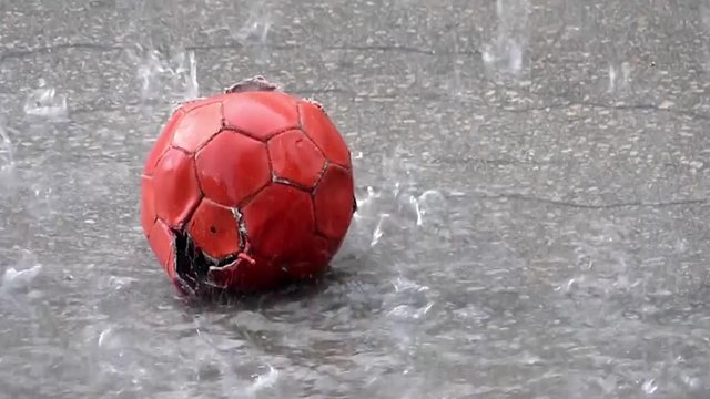 Torn red ball on street on rain