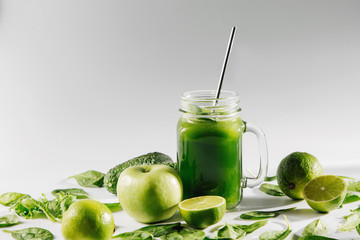 Healthy green smoothie with spinach and green fruits and vegetables on white table.