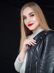 Fashion portrait stylish pretty blonde woman with bright trandy makeup red lips posing outdoor black backgrpound wearing a rock black style leather jacket on her shoulder having fun in city.