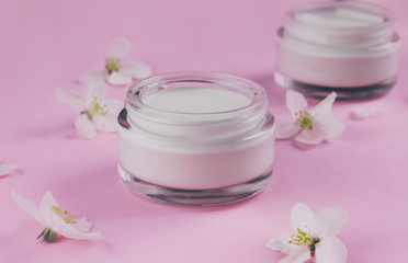 Fototapeta na wymiar Skin care beauty creams for the face with blooming flowers on pink background.