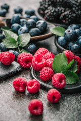 Fresh berries with raspberries, blueberries, blackberries in bowl on a stone stand on a dark metal background.