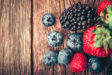 Fresh Summer Berries mix with Strawberry, Raspberry, Red currant, Blueberry and Blackberry on wood background.