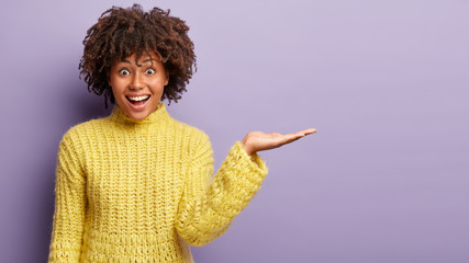 Positive female promoter raises palm over copy space, pretends holds something, wears yellow...