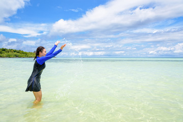 Happy asian teen girl in a swimsuit play splashing water in the sea with fun under the blue sky of Ko Ra Wi on tour vacation summer holiday at Ko Lipe island, Tarutao National Park, Satun, Thailand