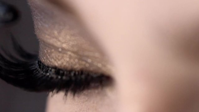Close-up apply mascara on eyelashes of beautiful female eye. Action. Incredible lash length with super curl effect by means black mascara for charming look