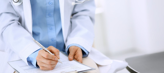 Female doctor writing up medication history records form on clipboard, while sitting at the chair. Physician at work in hospital or clinic. Healthcare, insurance and medicine concept