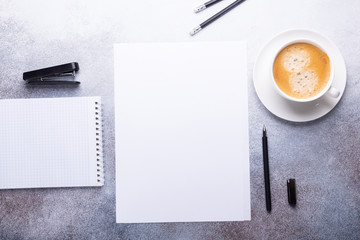 Office workplace with blank paper, cup of coffee, note pad and pen. Stone background. Top view