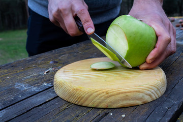 cutting with a knife a green apple on a wooden board
