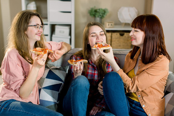 friendship, people, pajama party and junk food concept - happy young three women or girls eating pizza, popcorn and drinking wine at home